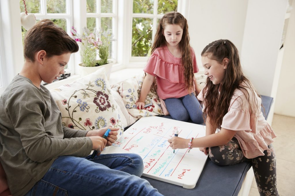 Children Making List Of Chores On Whiteboard At Home