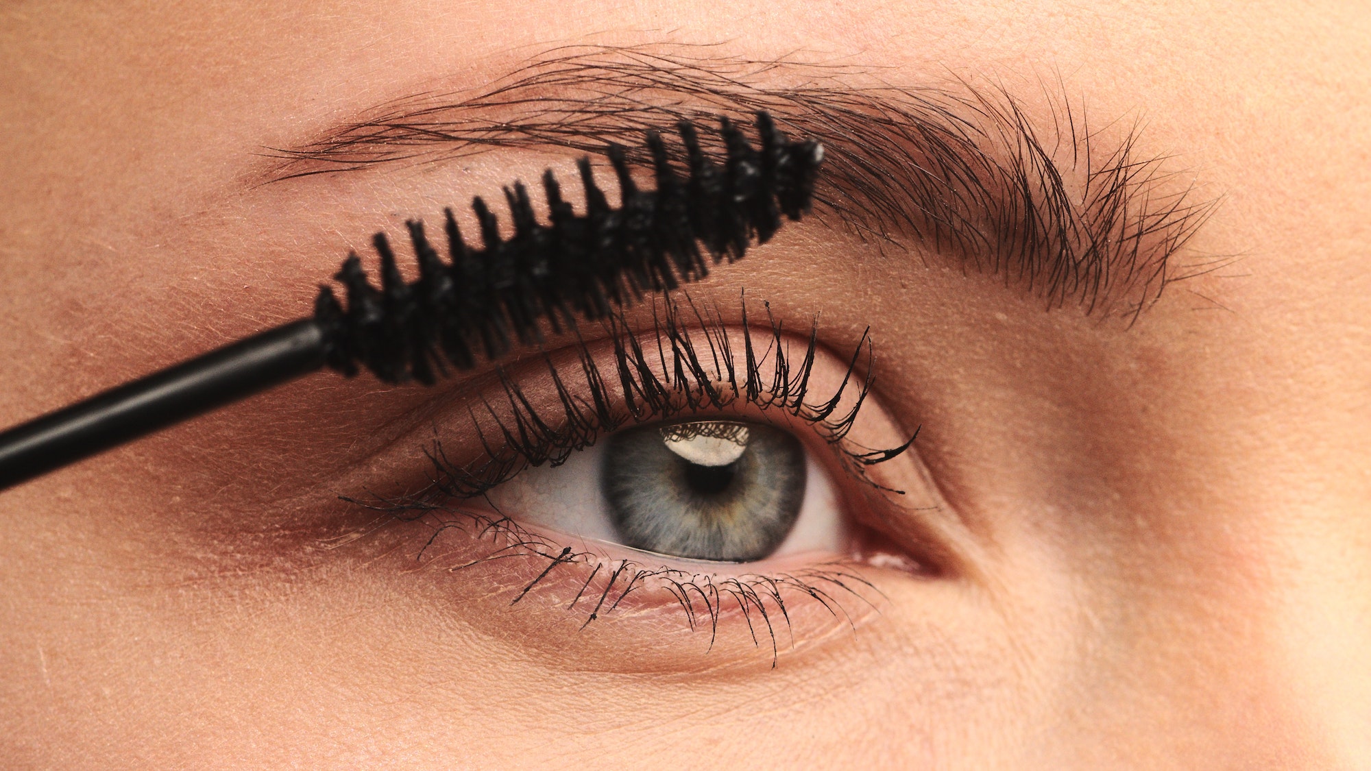 Closeup shot, stylist applies black mascara on the eyelashes of the female eye. Woman making makeup