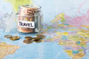 Travel budget concept. Money saved for vacation in glass jar on map background